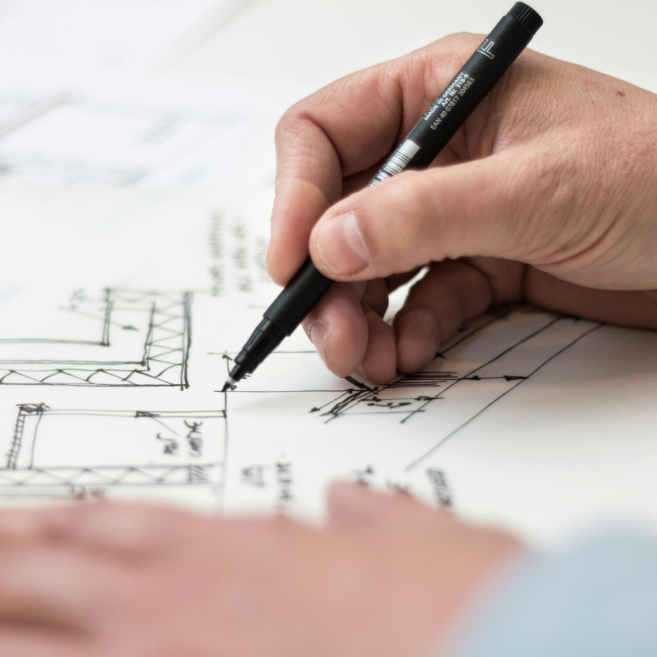 person holding a pen to a plan drawing adding detail