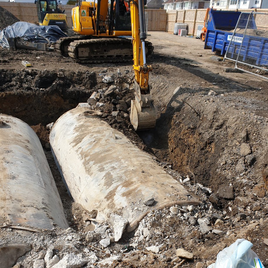 excavator removing soil around two below ground oil tanks before decommissioning